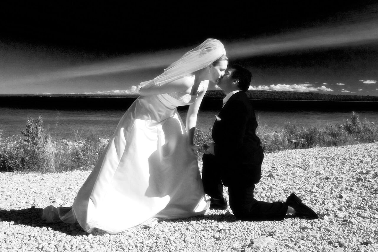 Black and white phjoto of bride kisssing groom on his knees